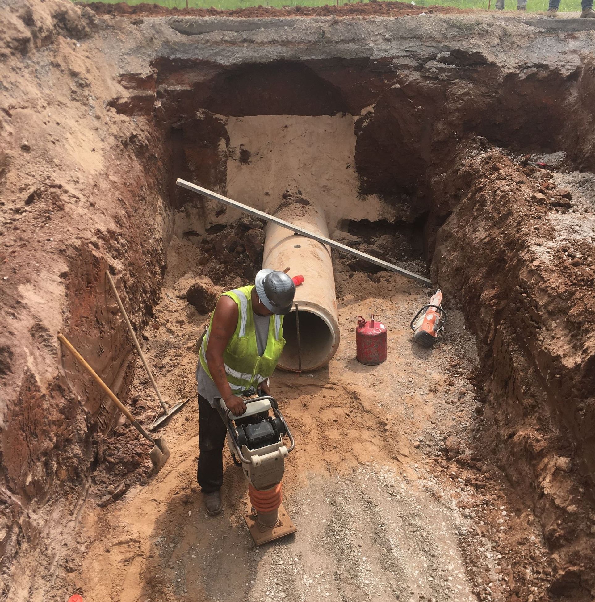 Worker using a rams foot to compact a bed for drainage pipe